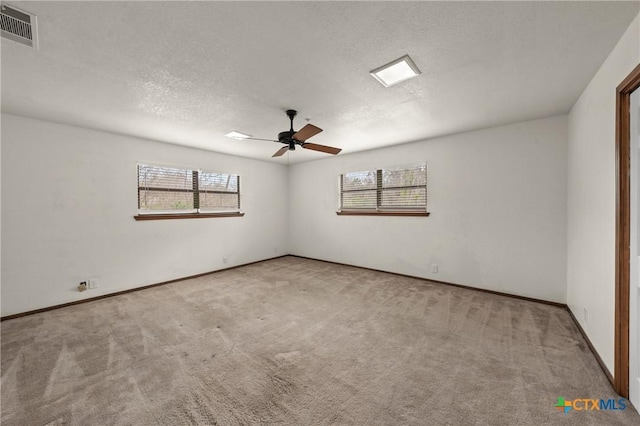 carpeted spare room with a ceiling fan, a wealth of natural light, visible vents, and a textured ceiling