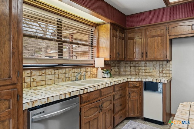 kitchen featuring light tile patterned floors, tile counters, backsplash, stainless steel dishwasher, and a sink