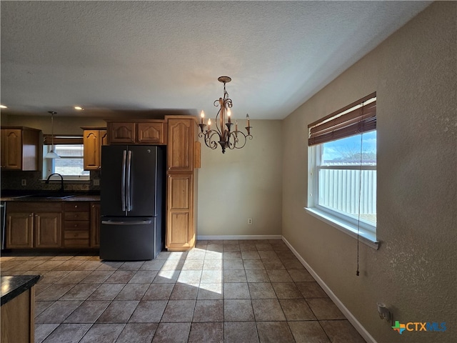 kitchen featuring stainless steel refrigerator, sink, a notable chandelier, pendant lighting, and decorative backsplash