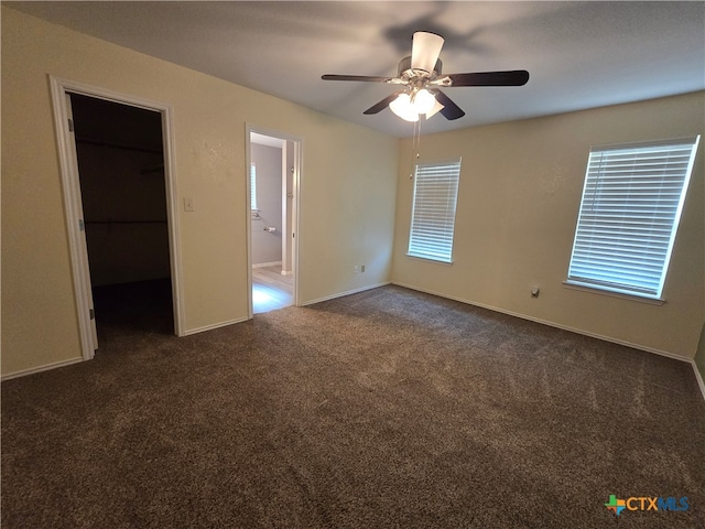 unfurnished bedroom with a closet, a spacious closet, dark carpet, ceiling fan, and ensuite bathroom