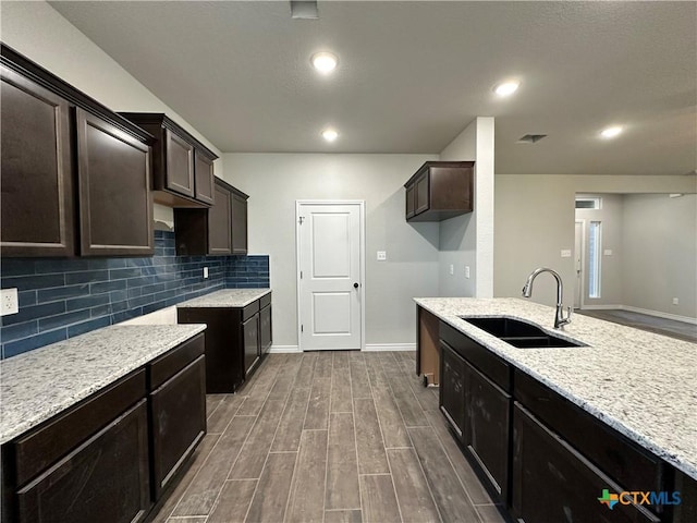 kitchen with backsplash, light stone counters, dark brown cabinetry, and sink