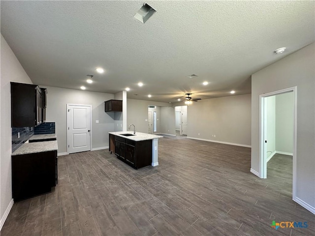 kitchen with a textured ceiling, ceiling fan, sink, and an island with sink