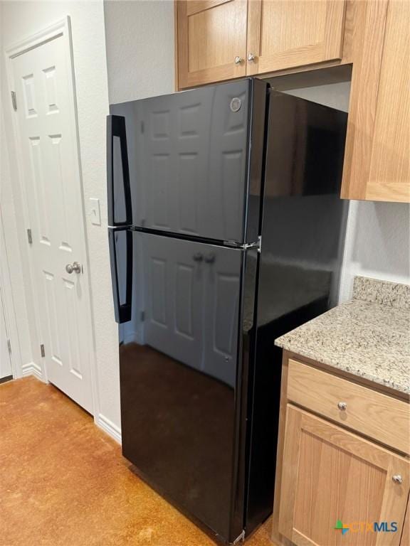 kitchen with light stone countertops, black fridge, and light brown cabinets