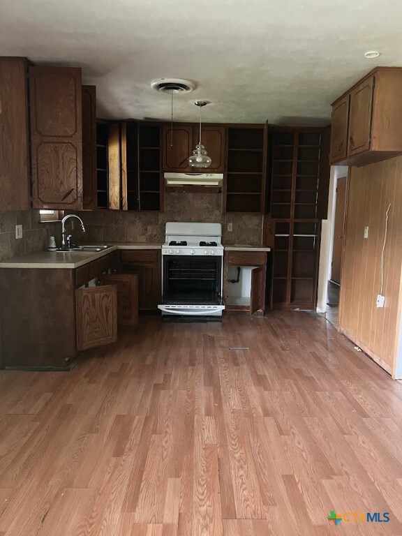 kitchen with white gas range, sink, dark brown cabinets, pendant lighting, and light wood-type flooring