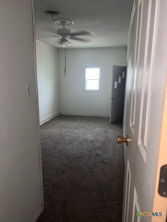 empty room with ceiling fan, a textured ceiling, and carpet