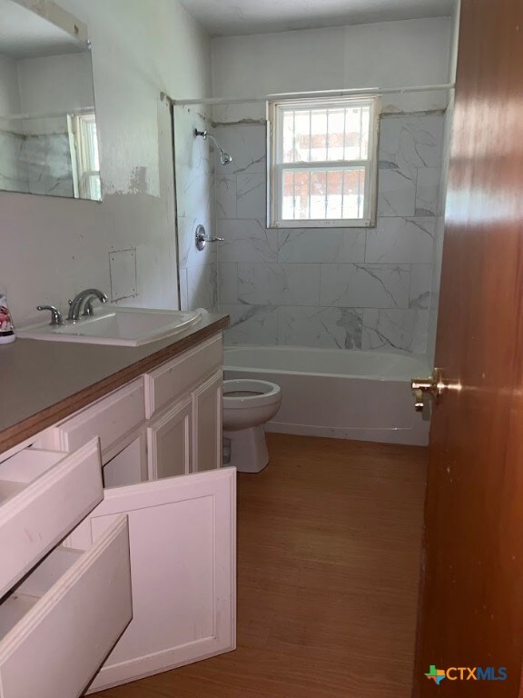 full bathroom with toilet, tiled shower / bath combo, vanity, and hardwood / wood-style floors