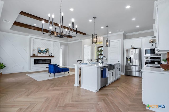 kitchen featuring a kitchen island with sink, light countertops, stainless steel appliances, open floor plan, and white cabinets