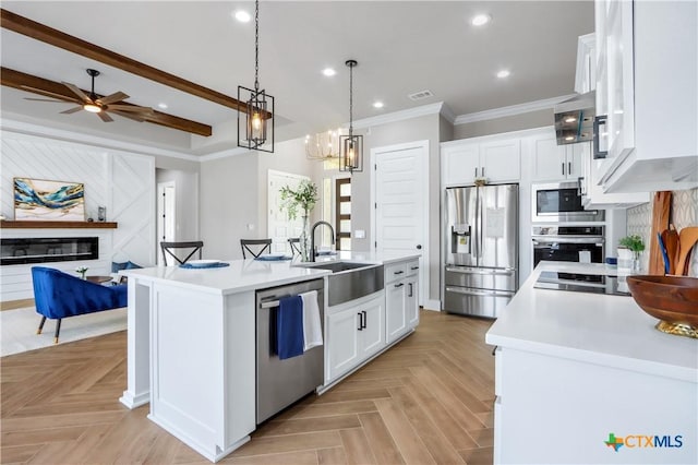 kitchen with stainless steel appliances, white cabinets, light countertops, and a kitchen island with sink