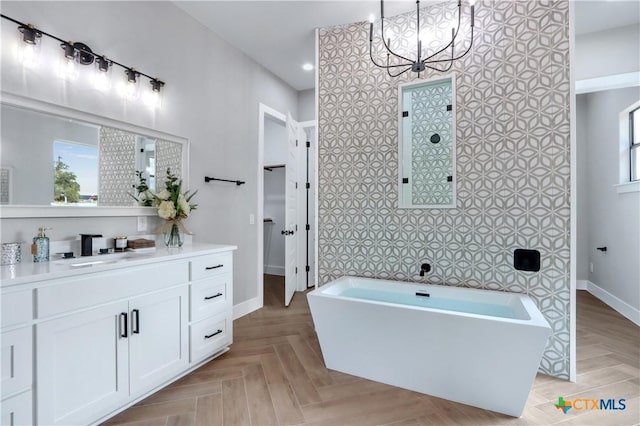 bathroom with baseboards, vanity, a freestanding bath, and a healthy amount of sunlight