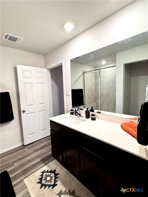 bathroom featuring a textured ceiling, vanity, hardwood / wood-style flooring, and a shower with shower door