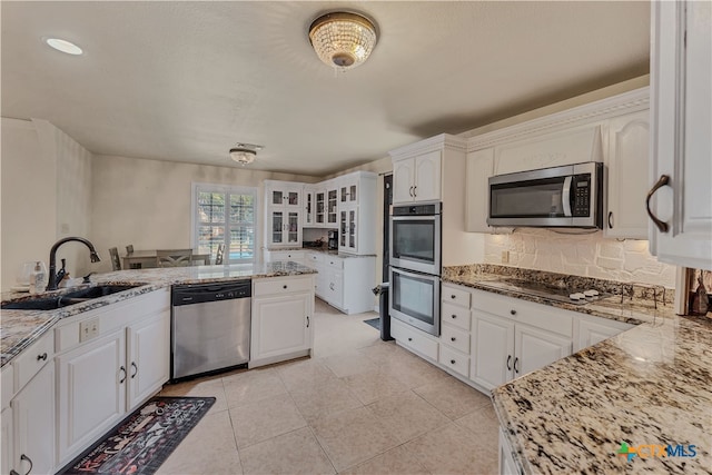 kitchen with stainless steel appliances, light tile patterned floors, sink, light stone countertops, and white cabinetry