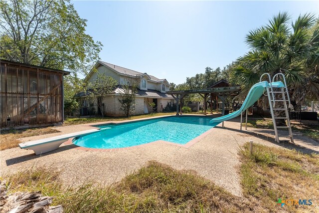 view of swimming pool with a water slide, a diving board, and a patio area