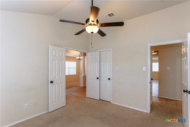 unfurnished bedroom featuring a closet, vaulted ceiling, light carpet, and ceiling fan with notable chandelier