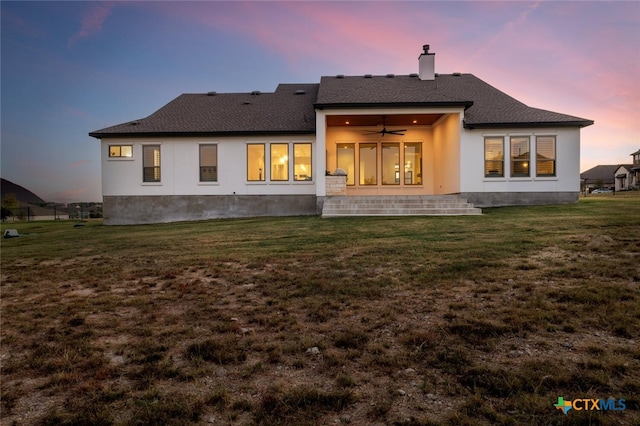 back house at dusk with ceiling fan, a lawn, and a patio area