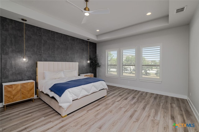 bedroom with light hardwood / wood-style floors, ceiling fan, and a tray ceiling