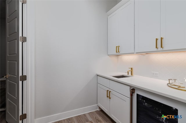 bar featuring tasteful backsplash, wine cooler, white cabinetry, light wood-type flooring, and sink