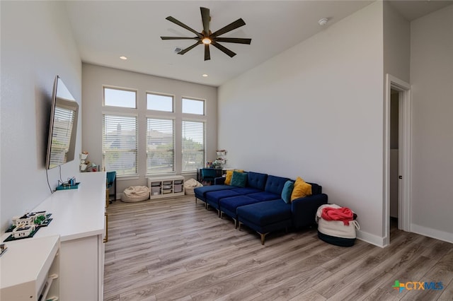 living room with light hardwood / wood-style floors, ceiling fan, and a high ceiling