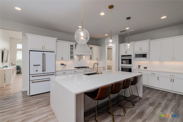 kitchen featuring white cabinetry, appliances with stainless steel finishes, hanging light fixtures, sink, and an island with sink