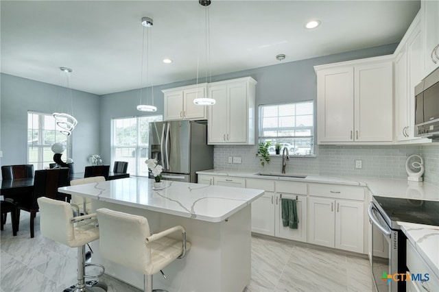 kitchen featuring stainless steel appliances, decorative light fixtures, sink, white cabinets, and a center island