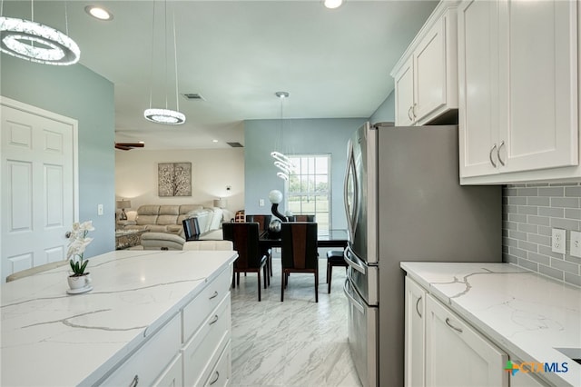 kitchen with stainless steel refrigerator, white cabinetry, pendant lighting, and light stone counters