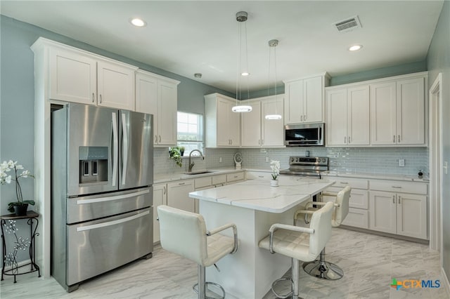 kitchen featuring appliances with stainless steel finishes, hanging light fixtures, sink, white cabinets, and a center island