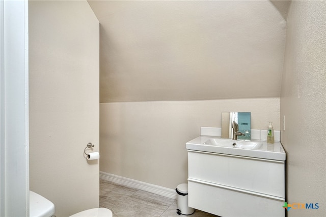 bathroom with toilet, lofted ceiling, vanity, and tile patterned floors