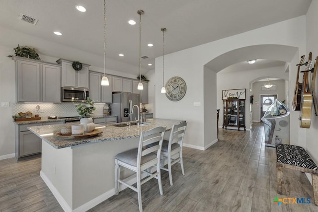 3214 Roan St, New Braunfels, TX 78130 - kitchen featuring gray cabinets, appliances with stainless steel finishes, arched walkways, a center island with sink, and light wood-style flooring