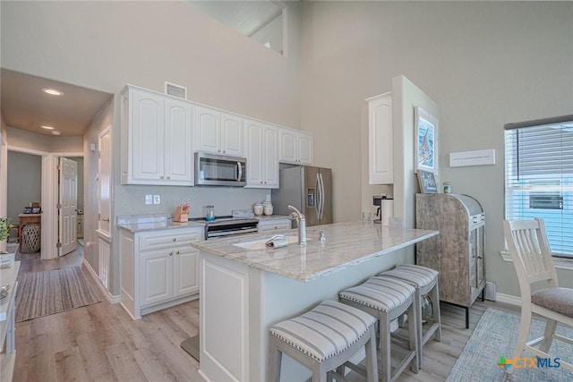 kitchen featuring visible vents, a kitchen bar, light stone counters, stainless steel appliances, and a sink