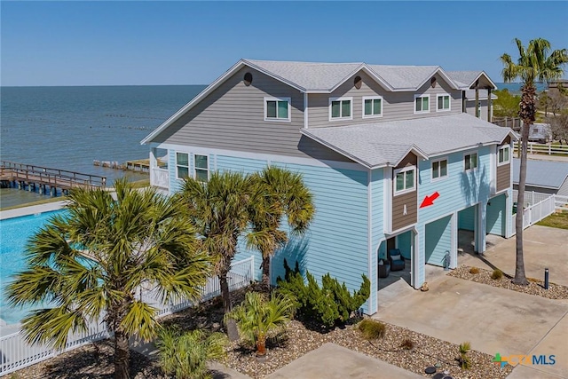 view of front of house featuring driveway, a shingled roof, fence, and a water view