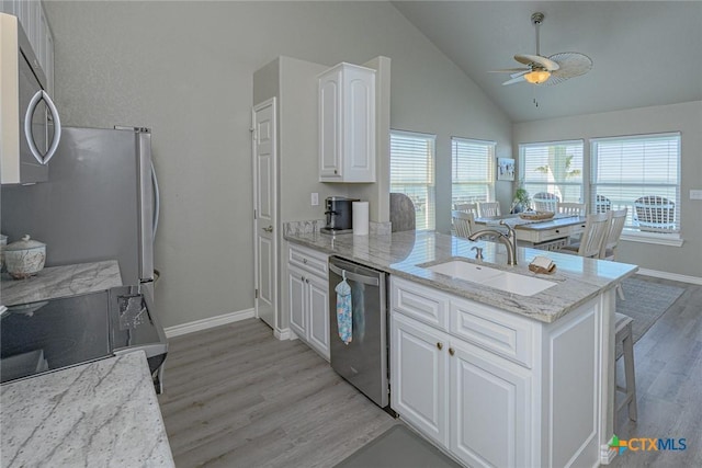 kitchen featuring a peninsula, a sink, appliances with stainless steel finishes, white cabinetry, and light wood-type flooring