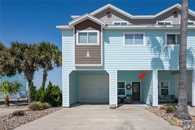 raised beach house featuring driveway, covered porch, and an attached garage