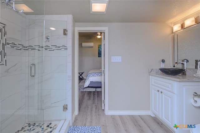 ensuite bathroom featuring an AC wall unit, a stall shower, wood finished floors, baseboards, and vanity