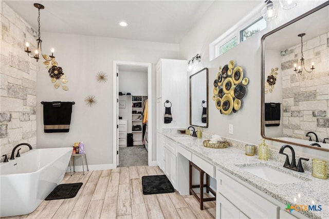 bathroom with a chandelier, a soaking tub, double vanity, and a walk in closet