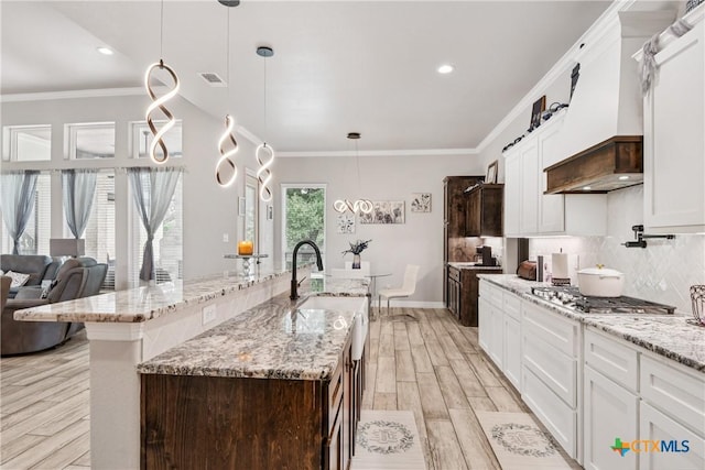 kitchen with light wood-style floors, tasteful backsplash, stainless steel gas stovetop, white cabinetry, and a center island with sink