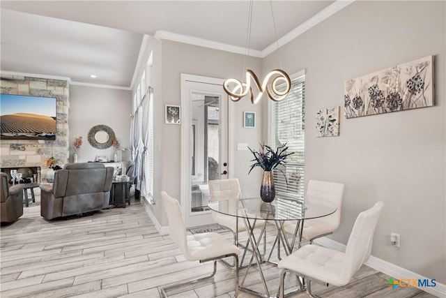 dining space featuring wood finished floors, ornamental molding, healthy amount of natural light, a fireplace, and a chandelier