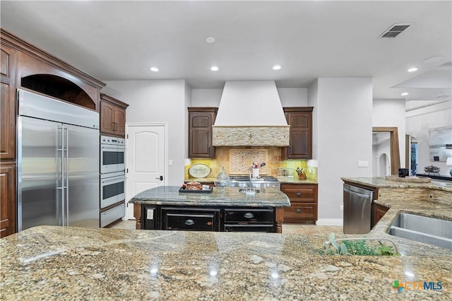 kitchen with custom exhaust hood, tasteful backsplash, a center island, appliances with stainless steel finishes, and light stone countertops