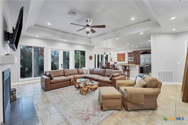 tiled living room with a tray ceiling, french doors, and ceiling fan