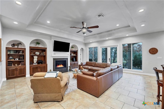 tiled living room featuring a raised ceiling, built in features, ceiling fan, and french doors