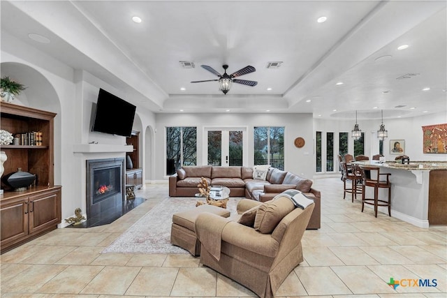 tiled living room featuring a raised ceiling, built in shelves, ceiling fan, and french doors