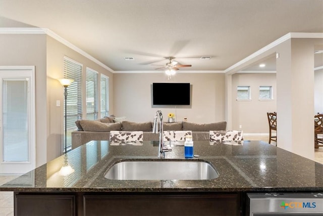 kitchen featuring a kitchen island with sink, sink, ornamental molding, and dark stone counters