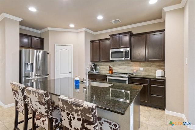 kitchen featuring appliances with stainless steel finishes, sink, dark stone countertops, dark brown cabinetry, and a center island with sink