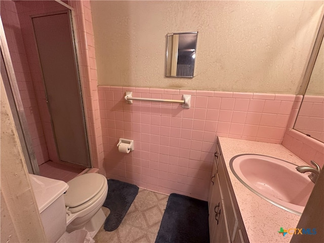 bathroom with tile walls, tile patterned floors, walk in shower, vanity, and toilet