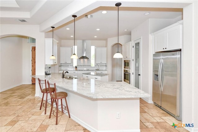 kitchen featuring wall chimney range hood, a sink, stone tile floors, stainless steel appliances, and backsplash