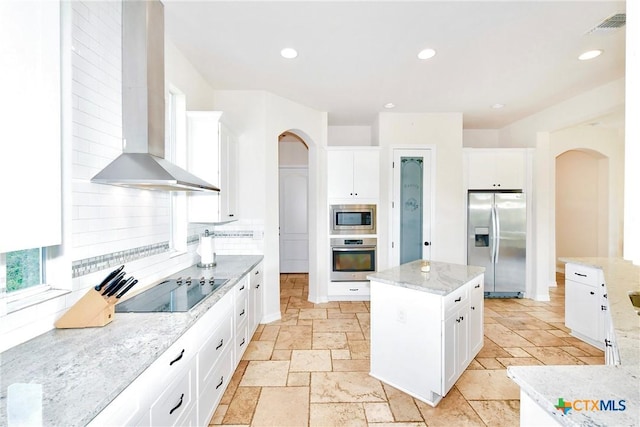 kitchen with arched walkways, stone tile flooring, wall chimney exhaust hood, and appliances with stainless steel finishes