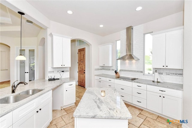 kitchen with wall chimney range hood, a sink, decorative backsplash, arched walkways, and visible vents