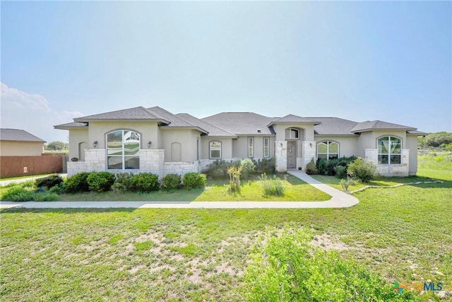 view of front facade featuring stone siding, a front yard, stucco siding, and fence