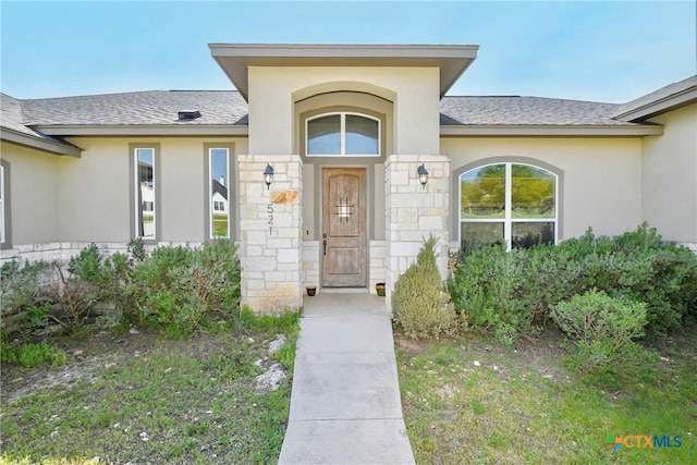view of exterior entry featuring roof with shingles and stucco siding