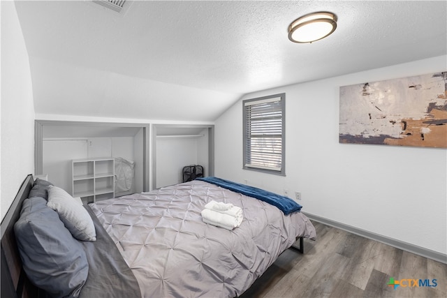 bedroom featuring hardwood / wood-style flooring, a textured ceiling, and lofted ceiling