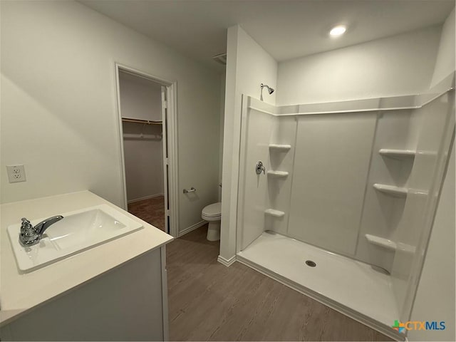 bathroom featuring toilet, a spacious closet, a shower stall, and wood finished floors