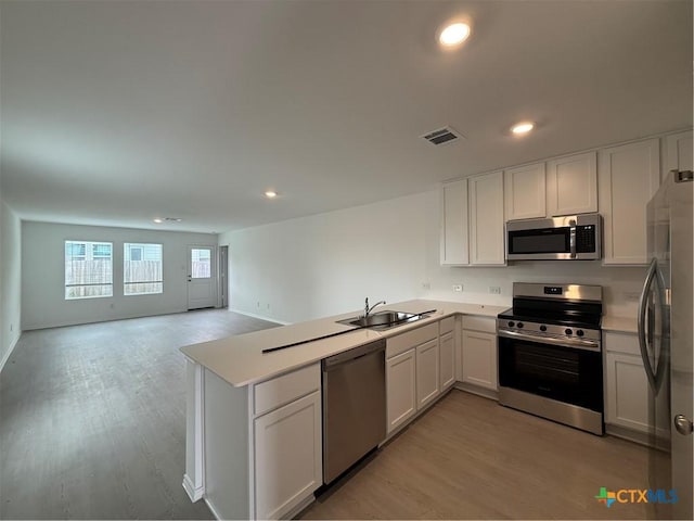 kitchen with visible vents, appliances with stainless steel finishes, a sink, a peninsula, and light wood-style flooring